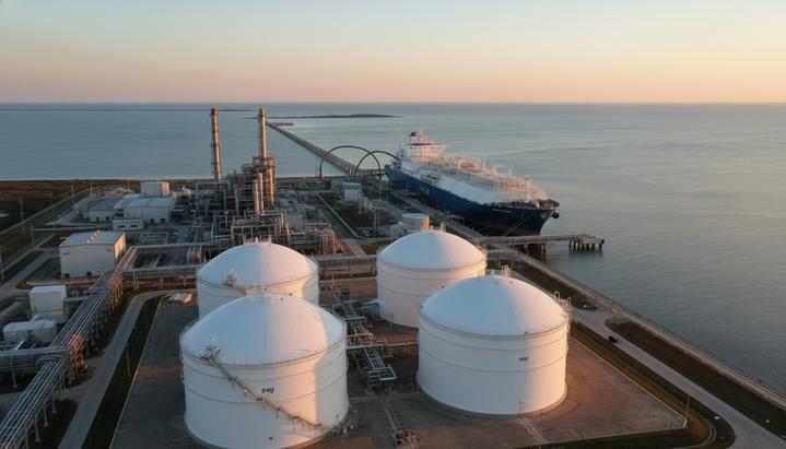 Современный терминал СПГ с криогенными резервуарами на берегу моря. У причала стоит крупный танкер-газовоз на рассвете.