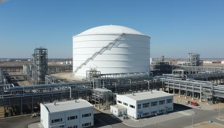 Крупный белый резервуар для хранения сжиженного природного газа (СПГ) на территории промышленного объекта с трубопроводами.