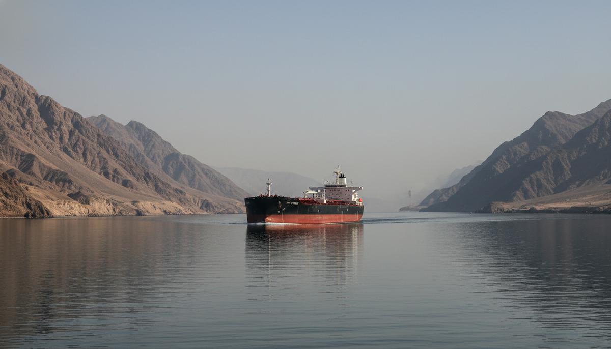 Одинокий нефтяной танкер проходит через узкий Ормузский пролив между скалистыми, засушливыми горами.